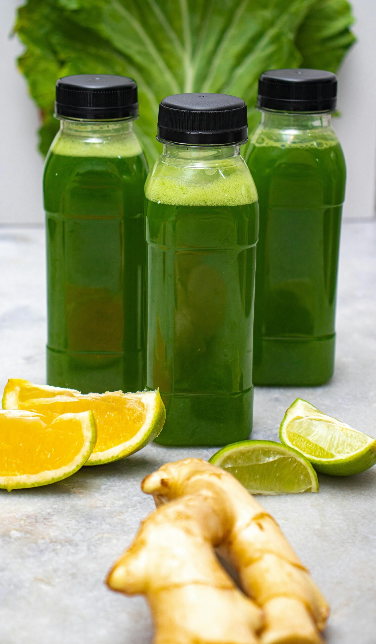Three bottles of refreshing green juice surrounded by citrus slices and fresh ginger.